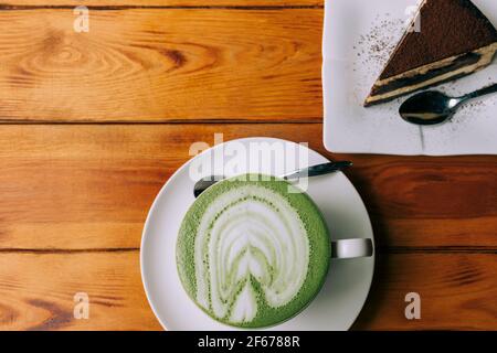 Une tasse de café matcha dans une grande tasse blanche au centre du cadre avec un gâteau sur une table en bois marron. Copier l'espace Banque D'Images