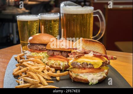 Assiette de hamburgers au fromage au bacon avec frites dans un restaurant de style restaurant avec un pichet de bière. Banque D'Images