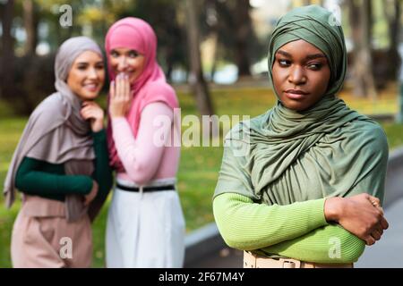 Femmes arabes Whispering derrière le dos de la femme musulmane noire en plein air Banque D'Images