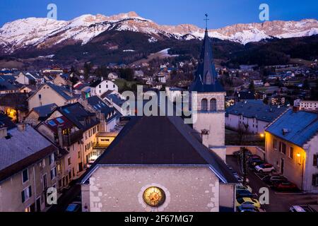 Vue aérienne de l'église avec tour dans le petit village en soirée. Montagnes enneigées à l'horizon, Vercors, France. Banque D'Images