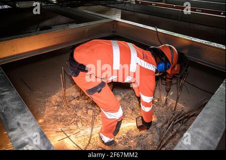 Vue arrière de l'ouvrier en costume de protection coupant les renforts en acier dépassant du béton. Jet d'étincelles chaudes sur le chantier. Banque D'Images