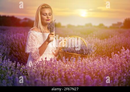 Belle jeune femme en robe blanche vaporeuse dans une lavande champ au coucher du soleil Banque D'Images