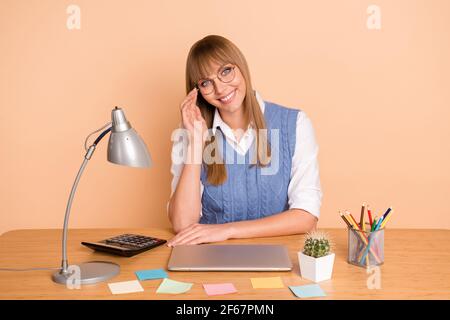 Photo portrait d'une femme en lunetterie bleu gilet souriant travaillant de chez vous isolé à distance sur un arrière-plan de couleur beige pastel Banque D'Images