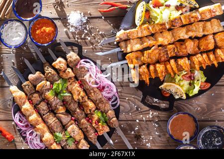 Émincé de kebab sur une brochette de métal avec sauce, tranches de concombres, tomates et oignons sur un plateau en bois Banque D'Images