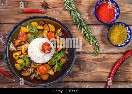 Riz sur une assiette de légumes mijotés sur un fond de bois décoré de romarin, de piment, d'épices. Service de restaurant. Banque D'Images