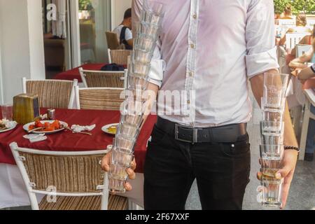Un serveur dans le restaurant de l'hôtel transporte deux pyramides de verres sales. Service de restaurant. Banque D'Images
