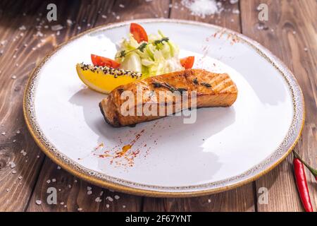 Poisson grillé sur une assiette de légumes, poivron, gros sel sur fond de bois brun. Service de restaurant. Banque D'Images