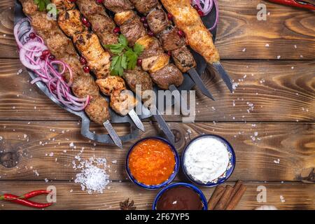 Émincé de kebab sur une brochette de métal avec sauce, tranches de concombres, tomates et oignons sur un plateau en bois Banque D'Images