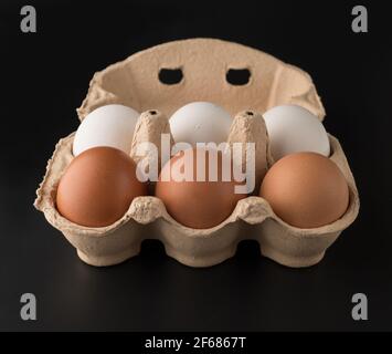 Oeufs de poulet, dans la quantité de six morceaux dans un plateau de papier jetable, sur un fond noir, isolé Banque D'Images