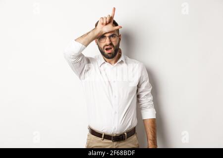 Un gars choqué montrant le signe perdant sur le front, se plaignant, se tenant sur fond blanc Banque D'Images