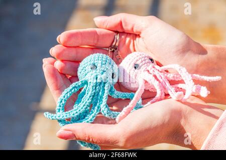 Porte-clés en tricot poulpe bleu et rose sur une main femelle gros-plan, porte-clés tricotés en peluche Banque D'Images