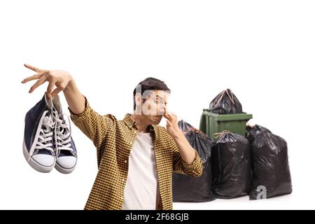 Guy jetant une paire de baskets odorantes dans les ordures isolées sur fond blanc Banque D'Images