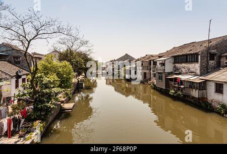 Tongli, Chine - 2 mai 2010: L'eau brune dans le canal avec l'architecture générique maisons blanches des deux côtés sous ciel bleu clair. Un peu de feuillage vert et ex Banque D'Images