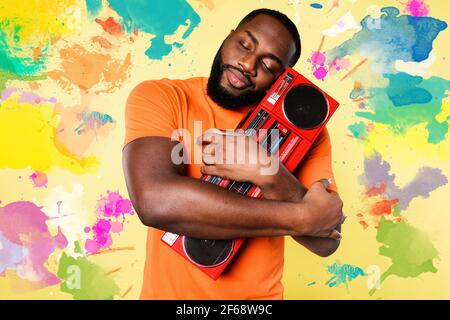 L'homme embrasse une vieille chaîne stéréo. Il aime la musique. Fond jaune Banque D'Images