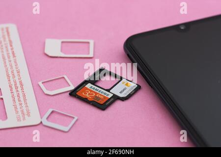 Gros plan de certaines cartes SIM (Orange) et mémoire (Samsung) pour téléphones mobiles à côté d'un smartphone sur fond rose Banque D'Images