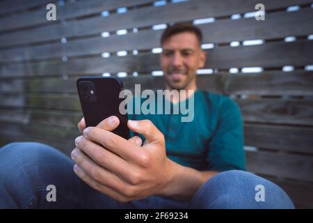 Homme ayant un appel vidéo facetime avec son smartphone noir moderne à l'extérieur. Regarder un smartphone Banque D'Images