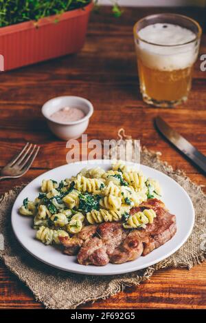 Steak de porc avec pâtes crémeuses aux épinards, garni de fromage râpé Parmesan sur plaque blanche Banque D'Images