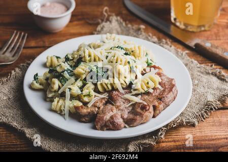 Steak de porc avec pâtes crémeuses aux épinards, garni de fromage râpé Parmesan sur plaque blanche Banque D'Images