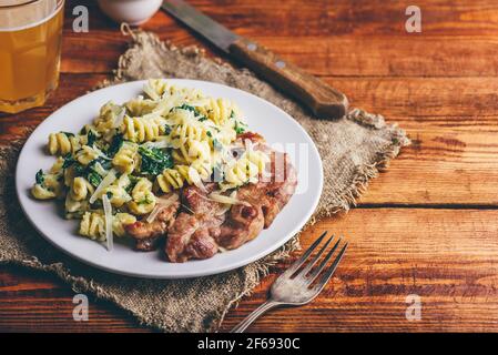 Steak de porc avec pâtes crémeuses aux épinards, garni de fromage râpé Parmesan sur plaque blanche Banque D'Images