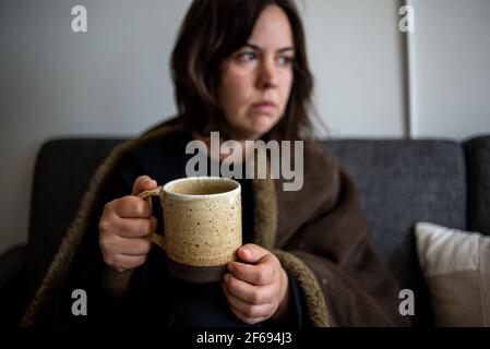 Détail de femme enveloppé dans une couverture contenant une tasse à café Banque D'Images