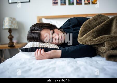Femme couchée sur le côté du lit sous une couverture Banque D'Images