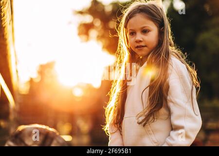 Petite fille blanche blonde a dans le parc, dans les rayons du soleil couchant. Photo de haute qualité Banque D'Images