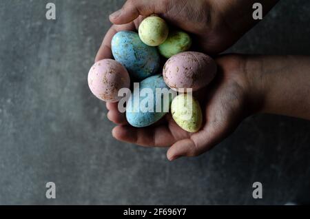 Œufs de Pâques dans les mains sur fond gris, vue du dessus Banque D'Images