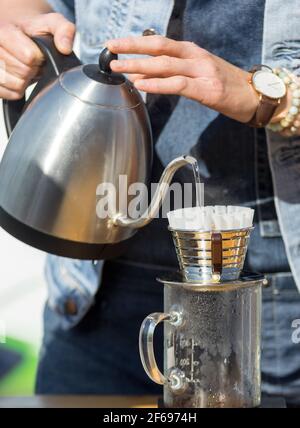 Préparation goutte à goutte, le barista prépare du café filtre frais au café extérieur. Premier jour de printemps avec un soleil chaud et lumineux après un long hiver. Banque D'Images