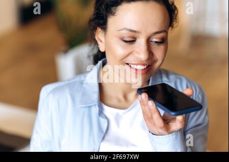 Conversation téléphonique, messagerie audio. Femme brunette de race mixte satisfaite, utilisant un smartphone, enregistrer des messages audio ou parler à des collègues ou à la famille sur le haut-parleur, regarder l'appareil, sourire amical Banque D'Images