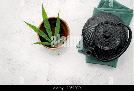 Théière d'époque avec thé à base de plantes de cannabis et feuilles de marijuana fraîches sur fond de béton. Banque D'Images