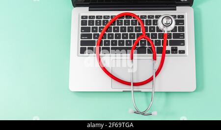 Vue de dessus du stéthoscope rouge sur le clavier de l'ordinateur portable, arrière-plan avec un bon espace pour les tasses. Concept de technologie et de médecine ou réparation d'équipements électroniques. Banque D'Images