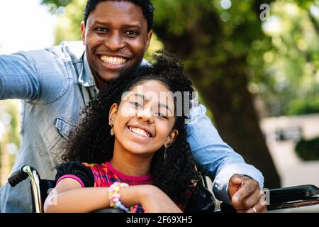 Petite fille en fauteuil roulant prenant un selfie avec son père. Banque D'Images