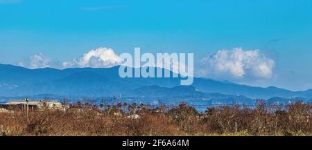 De vastes formations de nuages se coincent derrière une chaîne de montagnes au loin. Banque D'Images