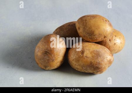 Cinq pommes de terre crues sur fond texturé jaune-gris. Mise au point sélective. Banque D'Images