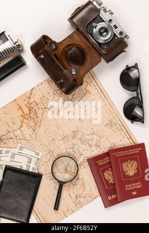 carte du monde, deux passeports, de l'argent dans un portefeuille en cuir noir, un ancien appareil photo dans un étui en cuir et des lunettes de soleil sur une table en bois blanc. vue d'abov Banque D'Images