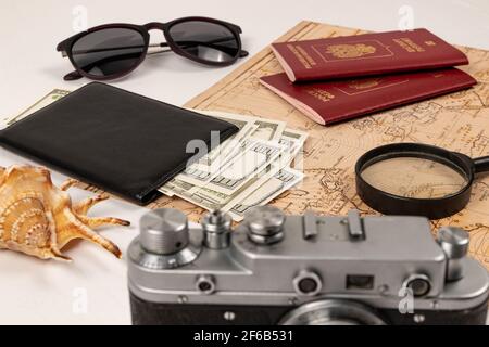 carte du monde, deux passeports, une loupe, de l'argent dans un portefeuille en cuir noir, un appareil photo à vieux film, des lunettes de soleil et une coquille sur une table en bois blanc Banque D'Images