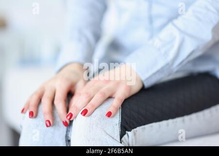 Les mains des femmes avec une manucure rouge couchée sur les genoux de près Banque D'Images