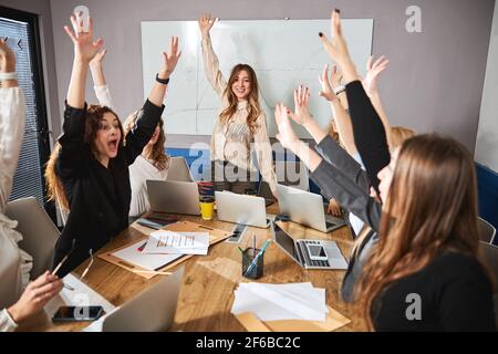 Une équipe créative et gaie se levant les mains pendant la réunion au bureau Banque D'Images
