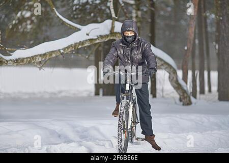 Activités de loisirs en hiver. Un adolescent vêtu d'un buff et de vêtements noirs fait un vélo en hiver. Banque D'Images