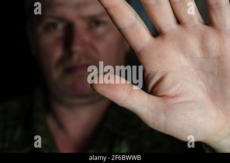 Prise de vue avec effet de flou. Homme en uniforme se protégeant de la caméra avec la main. Maless main gauche avec paume ouverte montre un geste de ses pieds. Un milieu Banque D'Images
