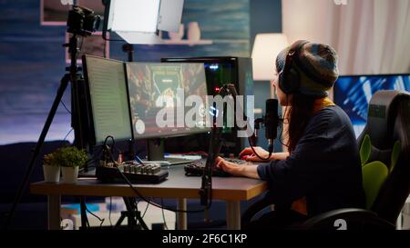 Femme streamer vérifiant le son à l'aide d'un mélangeur professionnel pour la diffusion de jeux vidéo en studio de jeu à domicile. Joueur professionnel jouant à des jeux vidéo de tir à la première personne discutant avec des coéquipiers sur le chat ouvert Banque D'Images