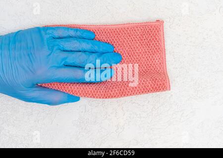 Une main dans un gant en caoutchouc bleu essuie la poussière d'un chiffon rose d'une surface en plâtre blanc, l'espace de copie. Maison, concept de ménage. Banque D'Images