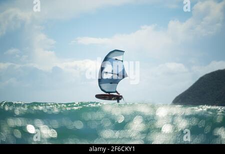 Une aile d'homme fait des feuilles en mer à l'aide d'une aile gonflable à la main, à cheval sur une planche de surf hydrofoil. Mer turquoise, ciel bleu ciel nuageux. Banque D'Images
