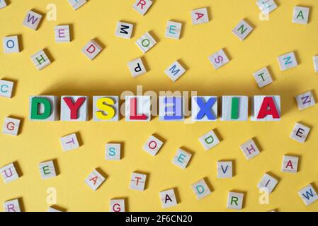 blocs d'alphabet en bois avec LE MOT DYSLEXIE au centre sur fond jaune. Concept de la sensibilisation à la dyslexie et du développement du cerveau humain Banque D'Images