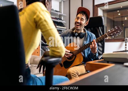 Photo de l'artiste heureux en studio de musique jouant la guitare à côté de la femme noire non reconnue. Banque D'Images