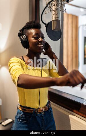 Photo de la belle femme noire chantant et utilisant le microphone dans un studio de musique.