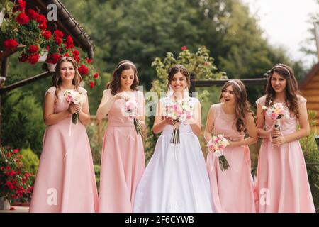 Bonne mariée avec demoiselle d'honneur tenir des bouquets et s'amuser dehors. Belle demoiselle d'honneur dans les mêmes robes stand par la mariée de charme dans la robe de mariage longue Banque D'Images