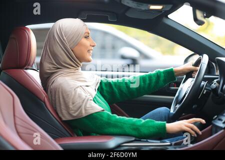 Une femme musulmane heureuse teste conduire une nouvelle voiture dans une ville urbaine Banque D'Images