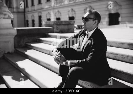 Hamdsome et le marié élégant se trouve sur les escaliers. Il porte des lunettes de soleil. Photo de mode en noir et blanc Banque D'Images