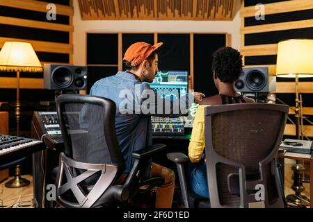 Photo d'un producteur de musique masculin travaillant avec un chanteur noir dans un studio de musique professionnel. Banque D'Images